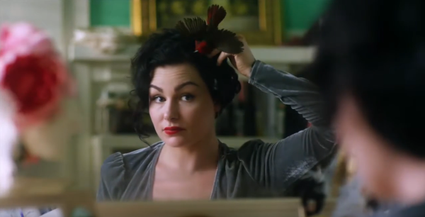 A white woman with a pin-up goth look adjusts a taxidermy bird fascinator in her hair.